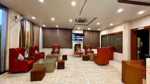 Un hall con sillas rojas, un televisor y una mesa de recepción.
