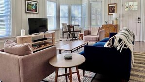 Ein Wohnzimmer mit Fernseher, Sitzgelegenheiten und Deckenventilator.