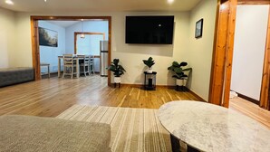 A spacious living room with a wooden floor, a marble coffee table, and a dining area with a white table and chairs.