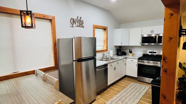 A modern kitchen with white cabinets, stainless steel appliances, a wooden dining table, and a hanging light fixture.