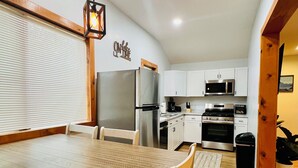 A modern kitchen with white cabinets, stainless steel appliances, and a wooden dining table.