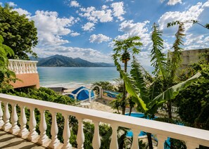 Vista costeira com piscina, praia e montanhas ao longe.