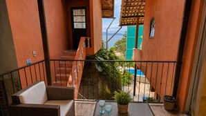 A balcony with wicker furniture, a small table with glasses, and a view of a pool and greenery.