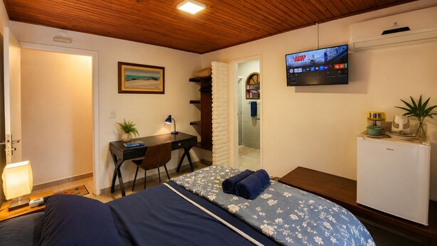 A bedroom with a bed, desk, chair, TV, and a small fridge.