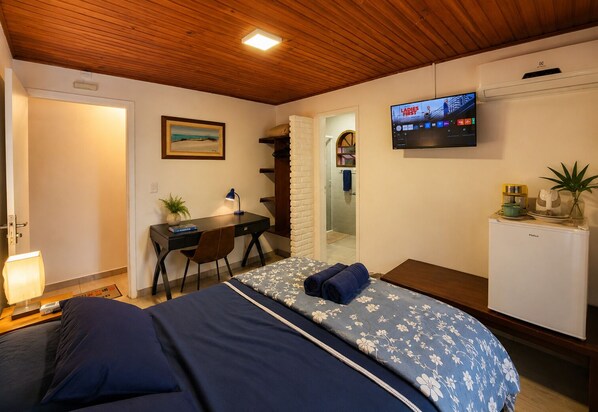 A bedroom with a bed, desk, chair, TV, and a small fridge.