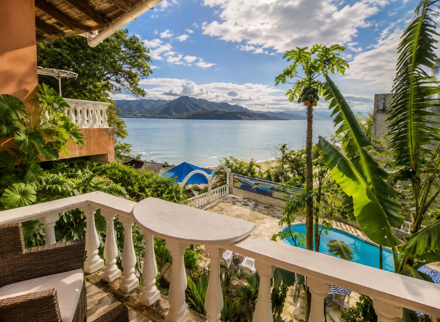 A balcony with a view of a swimming pool, a beach, and mountains.