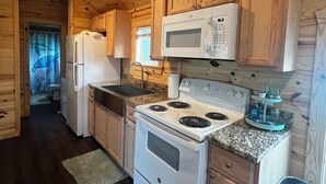 A compact kitchen with wooden cabinets, a white refrigerator, a microwave, a stove, and a sink.