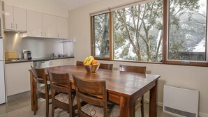 A modern kitchen with white cabinets, a built-in microwave, and a dining table with chairs. A bowl of fruit is on the table, and there is a window with a view of trees outside. - Golden Eagle 1 - Central Village (Central Village)