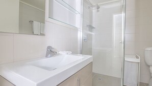 A modern bathroom with a white sink, mirror, and glass shower enclosure. - Golden Eagle 1 - Central Village (Central Village)