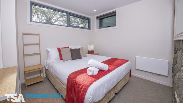 A bedroom with a bed, a nightstand, a bedside table, a ladder, and a window.