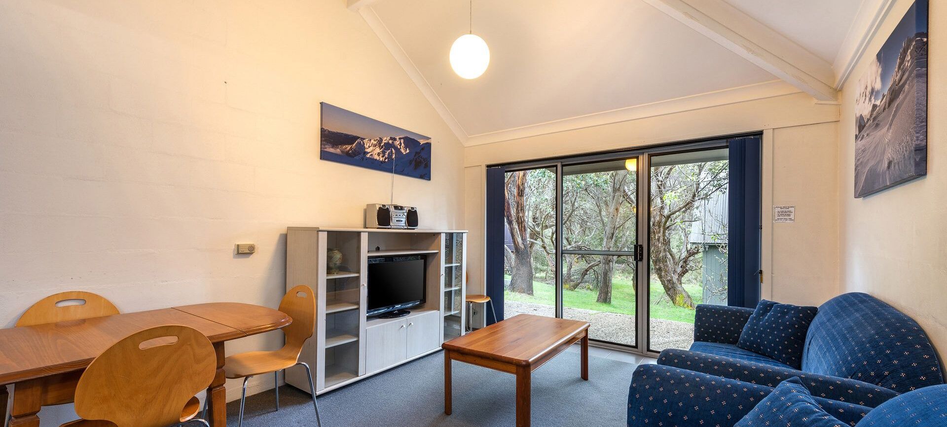 A cozy room with a wooden table, chairs, a blue sofa, a TV, and a bookshelf.