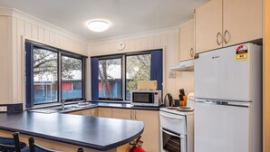 Une cuisine compacte dotée d’un four à micro-ondes, d’une cuisinière et d’un réfrigérateur intégrés, avec de grandes fenêtres et un plan de travail de couleur sombre.