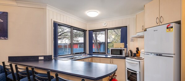 A compact kitchen with a built-in microwave, stove, and refrigerator, featuring large windows and a dark countertop.
