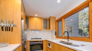 Eine moderne Küche mit Holzausstattung, einem Einbauofen, einer Mikrowelle und einem großen Fenster mit Blick auf Bäume.
