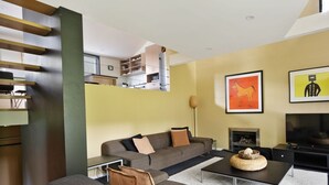 Un salon moderne avec un ensemble de canapés, une table basse et un téléviseur à écran plat. On y trouve une cheminée et des œuvres d’art accrochées au mur.