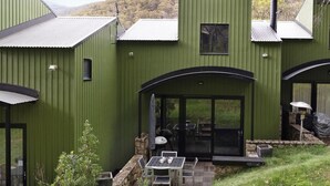 Un bâtiment moderne à l’extérieur verdoyant, doté d’un patio couvert avec des sièges extérieurs et offrant une vue sur le paysage environnant.