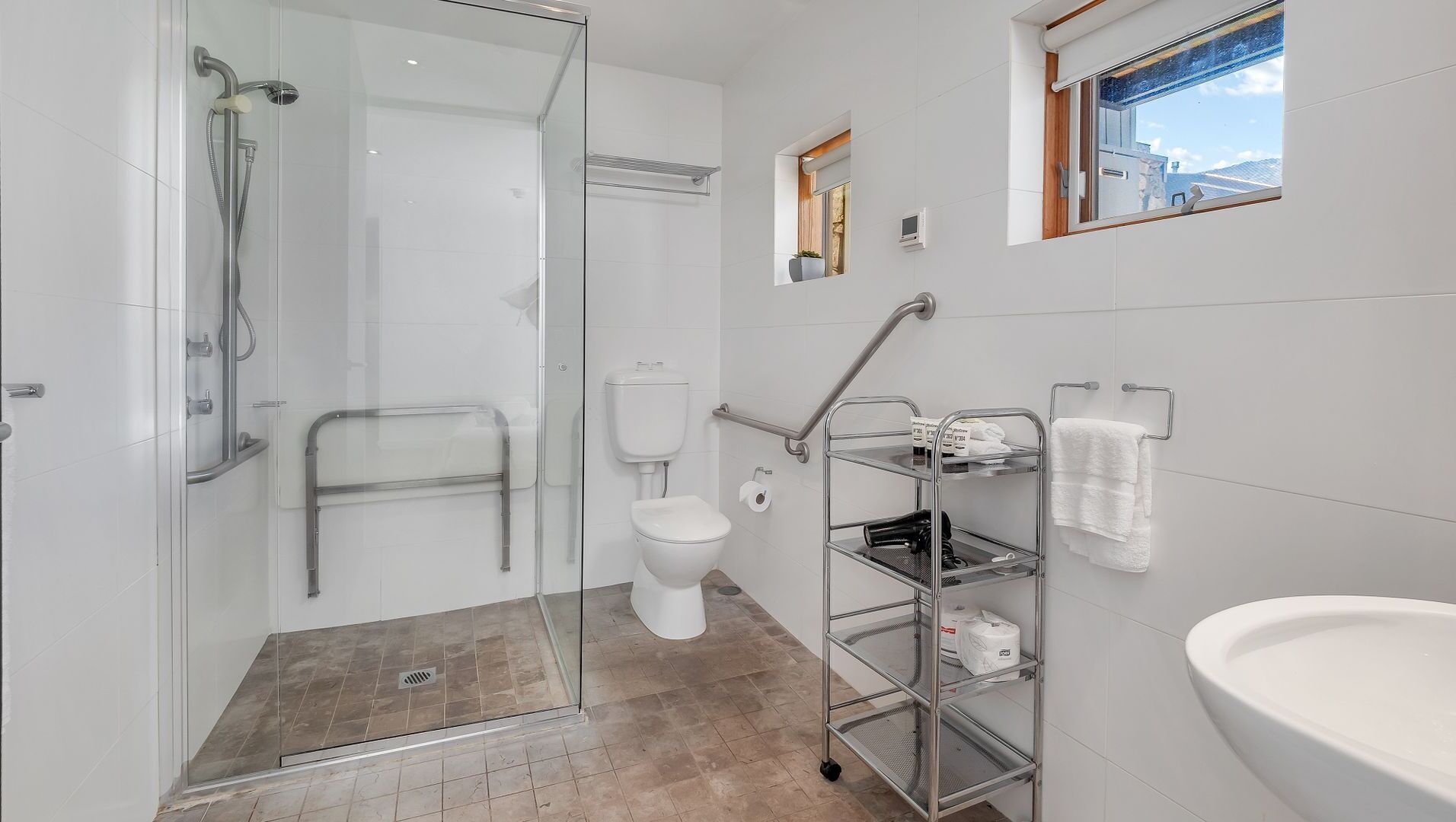 Un baño moderno con cabina de ducha de vidrio, inodoro, lavabo y estante con toallas.