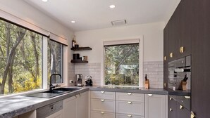 A modern kitchen with a large window, built-in appliances, and a dark wood cabinet. - Ridge Creek 1 - Crackenback Ridge (Ski-In-Ski-Out)