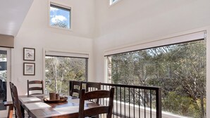 A dining area with a large table, chairs, and a view of trees through large windows. - Ridge Creek 1 - Crackenback Ridge (Ski-In-Ski-Out)