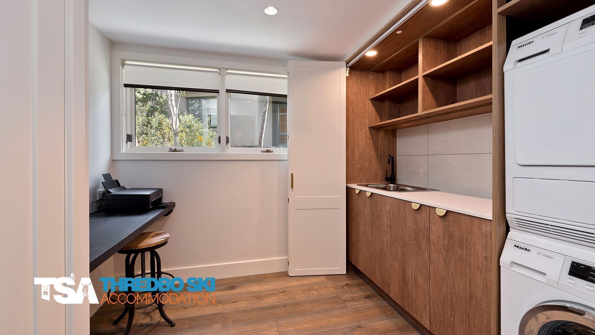 Cocina compacta con lavadora, un pequeño comedor con taburetes y una ventana que deja entrar luz natural.