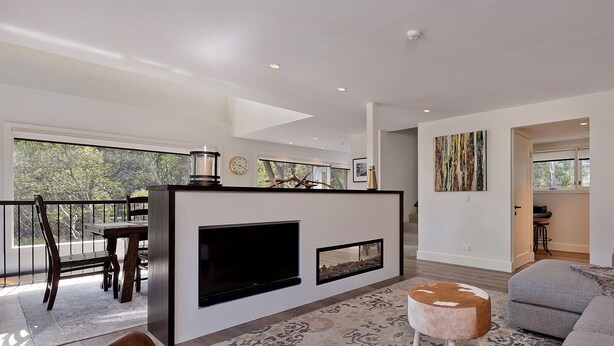 A modern living room with a flat-screen TV, a fireplace, a sofa, and a dining area with a table and chairs. - Ridge Creek 1 - Crackenback Ridge (Ski-In-Ski-Out)
