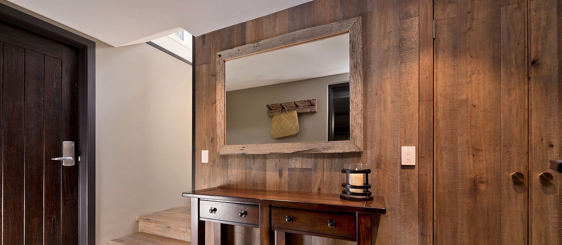 A wooden wall with a mirror, a small wooden cabinet, and a candle holder.