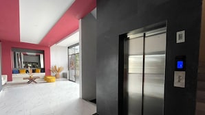 A modern elevator with a digital display, a marble-tiled floor, and a seating area with a sofa and yellow ottoman. - K Hotel (León)