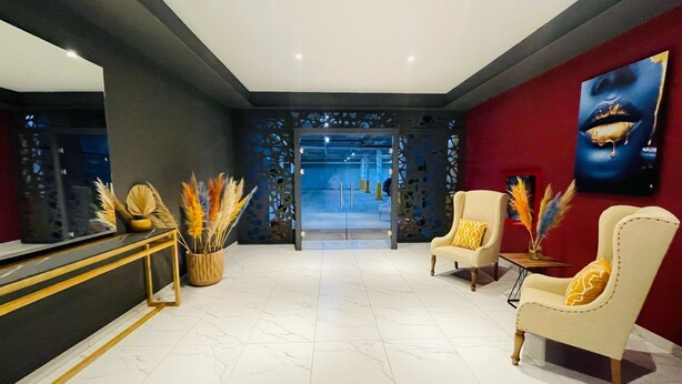 A modern lobby with a reception desk, two armchairs, a large mirror, and a red accent wall with a painting. - K Hotel (León)