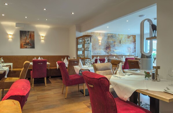 A restaurant with wooden flooring, red upholstered chairs, and white tablecloths. - Hotel & Restaurant Traube (Kallstadt)