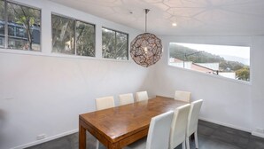 Comedor con mesa de madera, sillas blancas, ventanas amplias y una lámpara de techo geométrica.