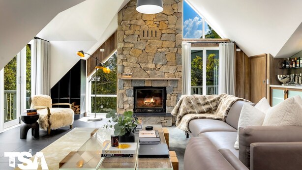 A spacious living room with a stone fireplace, a leather sofa, a glass coffee table with books and a plant, and a modern lamp. - Sequoia 5 Penthouse - Central Village (Central Village)