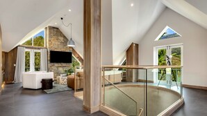 A spacious living area with a stone fireplace, a balcony with a glass railing, and a large window offering a view of the outdoors. - Sequoia 5 Penthouse - Central Village (Central Village)