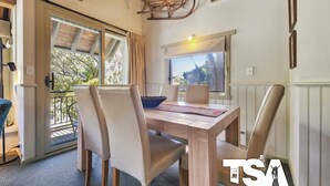 Un coin repas avec une table en bois, des chaises de couleur beige et une vue sur la verdure à l’extérieur.
