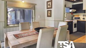 Un coin repas avec une table en bois, quatre chaises et une fenêtre équipée de stores.