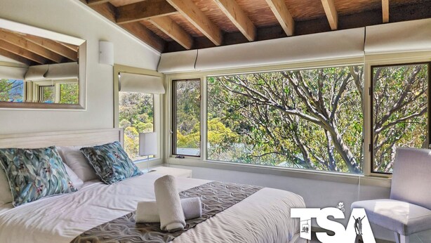 Une chambre avec une grande fenêtre, un lit, une chaise et un plafond en bois.