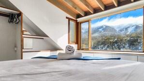 A bedroom with a large bed, a view of snow-covered mountains, and a wooden ceiling. - Sneznik - Central Villaage (Central Village)