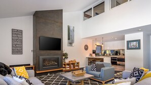 A modern living room with a fireplace, a television, and a kitchen in the background. - Snowbound Chalet 3 - Crackenback Ridge (Crackenback Ridge)