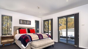 A bedroom with a bed, a nightstand, a desk, and a large sliding glass door to a balcony. - Snowbound Chalet 3 - Crackenback Ridge (Crackenback Ridge)