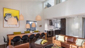 A modern living room with a dining area, a sofa, and a kitchen in the background.