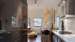A modern kitchen with a dining area, featuring a large island, pendant lights, and a view of the outdoors.
