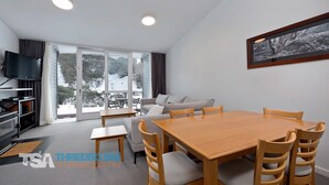 A modern hotel room with a dining area, a sofa, a TV, and a large window.