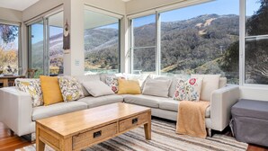 Ein modernes Wohnzimmer mit einer großzügigen Eckcouch, einem Holztisch und Blick auf eine Berglandschaft durch große Fenster.