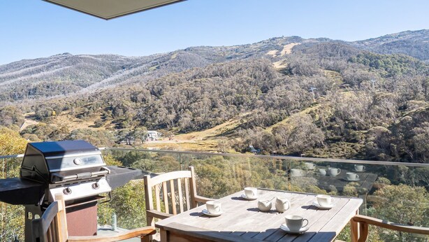 Ein Balkon mit Grill, Tisch und Stühlen mit Blick auf eine Berglandschaft.