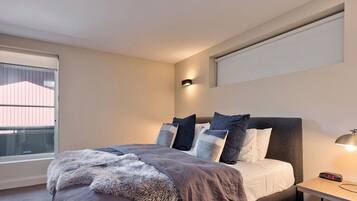 A bedroom with a bed, a bedside table with a lamp, a window, and a wall-mounted light.