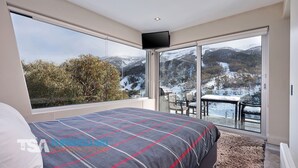 A bedroom with a large window, a bed, and a view of a snowy landscape. - The Peak 6 - Central Village (Central Village)