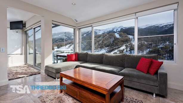 A modern living room with a large sectional sofa, a wooden coffee table, and a view of snow-covered mountains through large windows. - The Peak 6 - Central Village (Central Village)