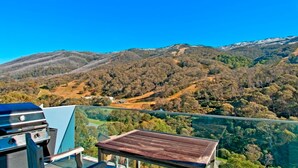 A balcony with a clear view of a mountainous landscape, a barbecue grill, and a wooden table. - The Peak 6 - Central Village (Central Village)