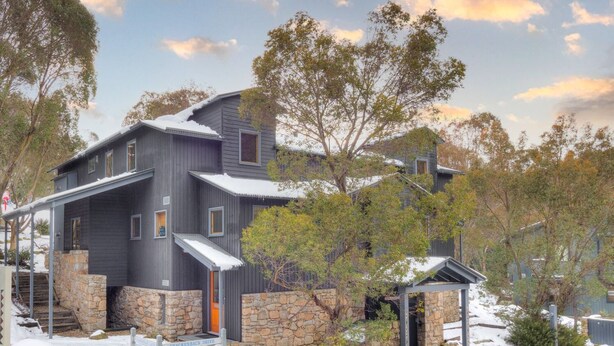 Une maison moderne à deux étages, avec des fondations en pierre et un toit en métal.