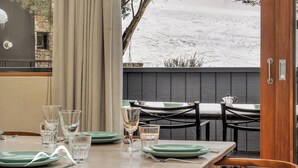 Un coin repas avec une table dressée pour quatre personnes, une vue sur un paysage enneigé et une porte en bois.