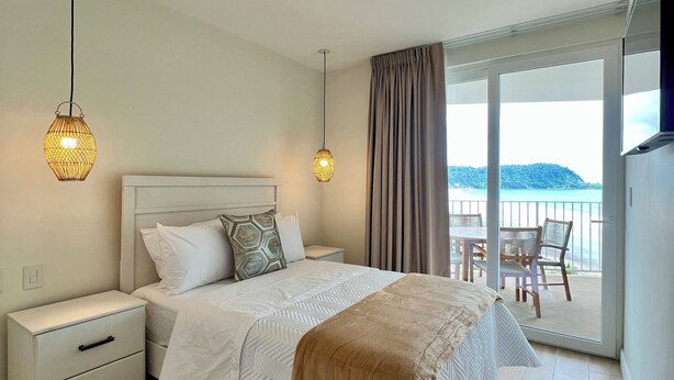 Un dormitorio con cama, mesitas de noche, una lámpara de techo y un balcón con vistas al mar.